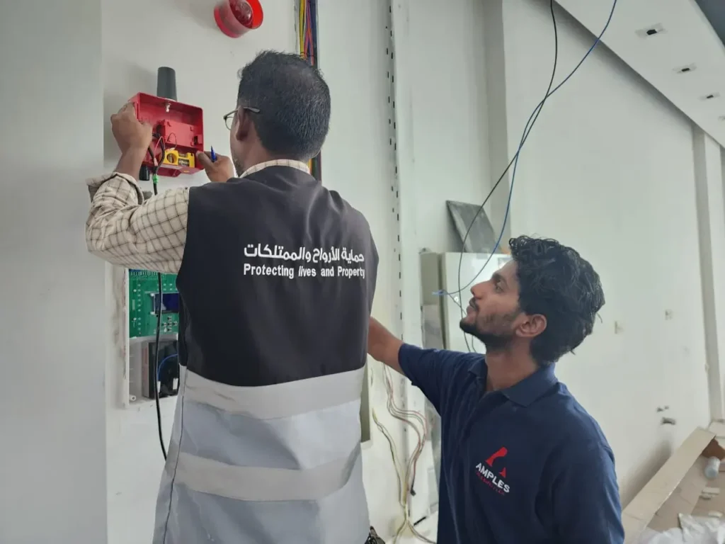 Two technicians installing a fire alarm system on a wall.