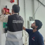Two technicians installing a fire alarm system on a wall.